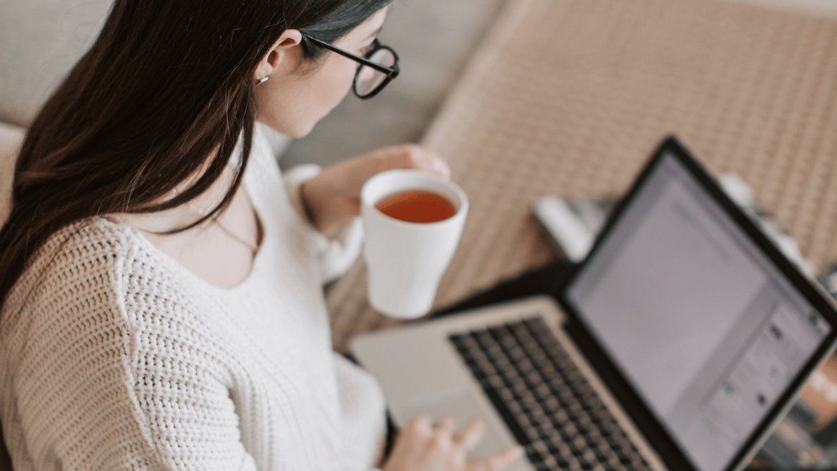 millennial woman working on her laptop while sitting on the floor with a cup of tea